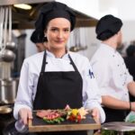 female Chef  in hotel or restaurant kitchen holding grilled beef steak plate with vegetable decoration