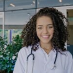 Latin young female doctor wear white uniform, white medical coat, stethoscope and looking at camera